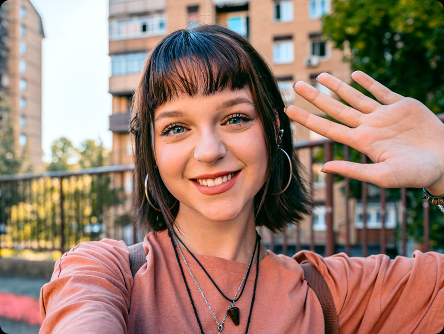 Eine Person macht drauen ein Selfie und trgt dabei ein pfirsichfarbenes Shirt sowie mehrere Halsketten. Dies unterstreicht die Fhigkeit der Frontkamera, beeindruckende Selfies aufzunehmen.