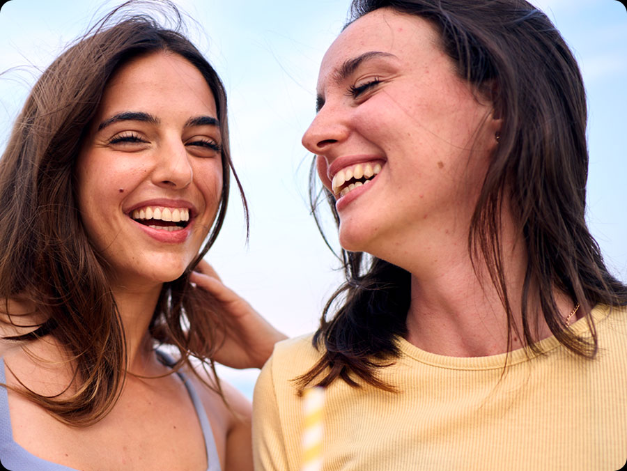 Zwei Personen stehen dicht beieinander im Freien. Eine trgt ein hellblaues, rmelloses Oberteil, die andere ein gelbes, kurzrmeliges Hemd. Dies unterstreicht die Super-HDR-Funktion des Galaxy S25 FE.