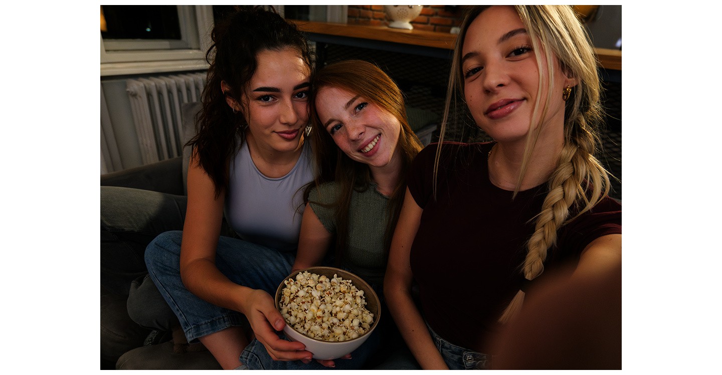 Drei M�dchen sitzen zuhause auf einem Sofa in einer schwach beleuchteten Umgebung und machen gemeinsam ein Foto. Eines der M�dchen nimmt das Foto mit dem Galaxy A37 5G auf, das mit Nightography f�r helle, lebendige Fotodetails sorgt.

    